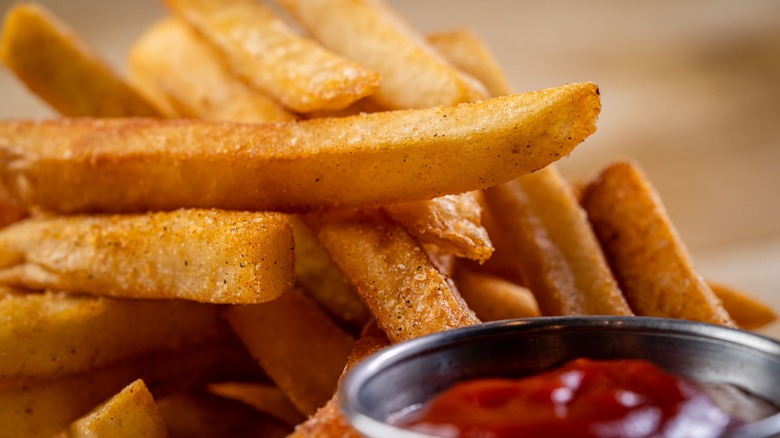 Crisp, perfectly seasoned french fries are piled high in front of a ketchup ramekin.