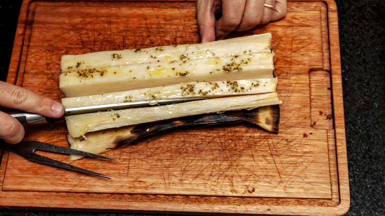 A hand holds a knife while slicing hearts of palm into strips on a cutting board
