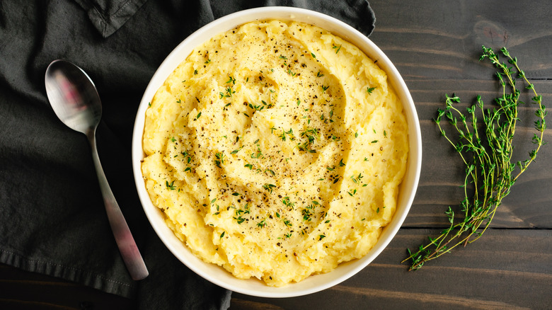 A large bowl of creamy, fluffy mashed potatoes topped with minced thyme leaves and crushed black pepper