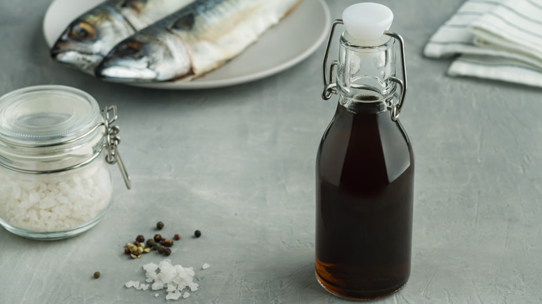 bottle of fish sauce with two fish on a plate in background