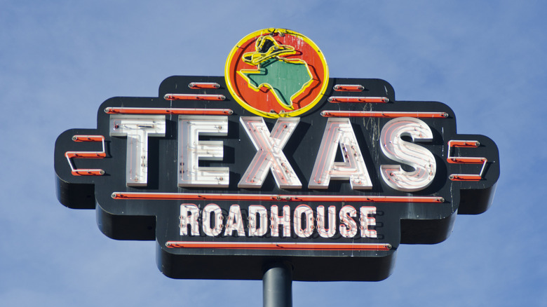 A Texas Roadhouse sign in front of a blue sky.
