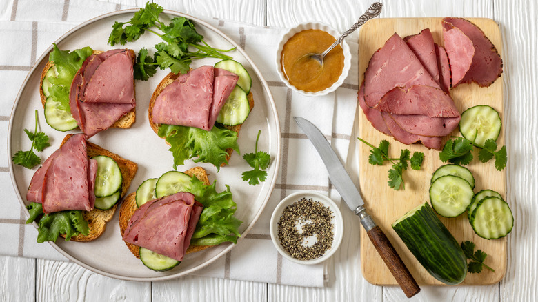 Open-faced corned beef sandwiches on plate next to bowls of mustard and pepper