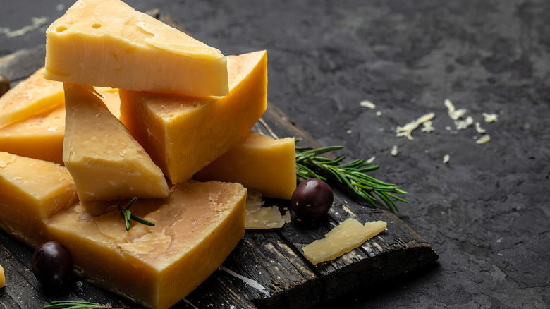 Slices of parmesan cheese on a wooden board with olives and herbs