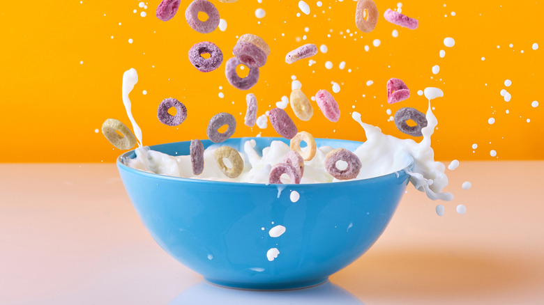 Fruity loops being poured into a splashing bowl of milk on a yellow and pink background