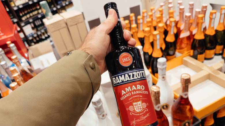 A man holding a bottle of amaro out above a display of champagne
