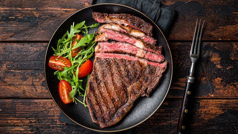 Grilled, sliced ribeye steak with salad on black plate