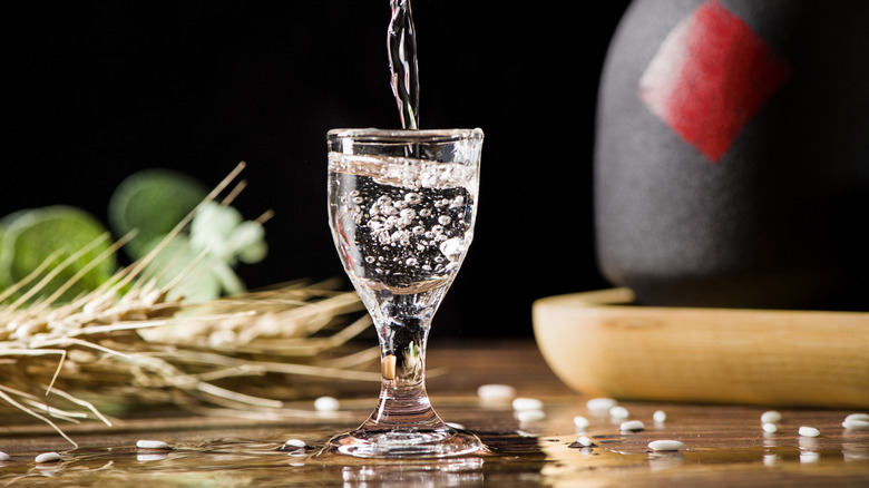 Baijiu being poured in small glass with black bottle in background.