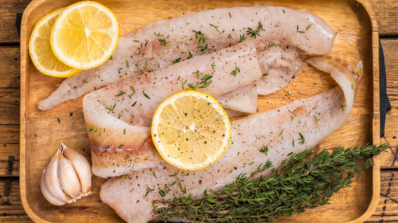 raw hake fillets on wooden board with lemon and herbs