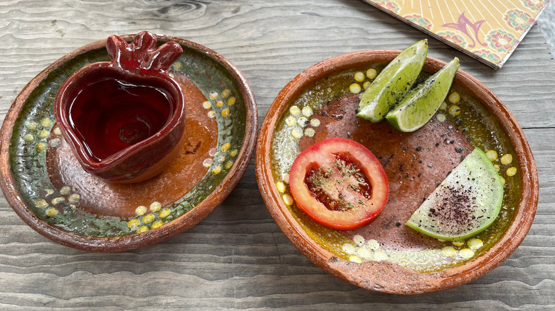 A shot of sotol in a ceramic cup on a plate next to a plate with lime and tomato slices