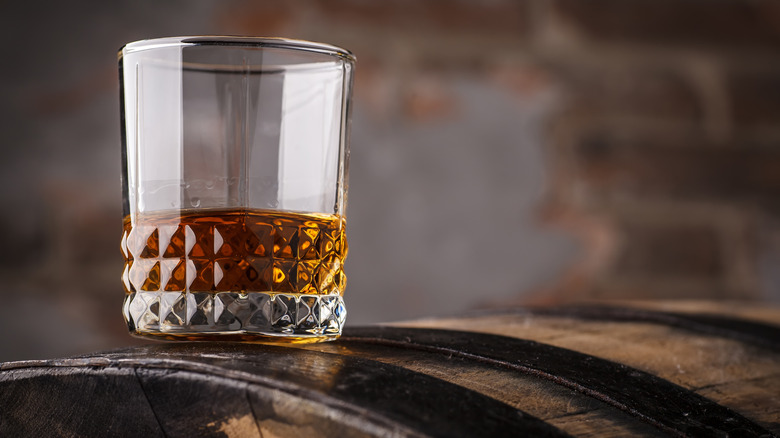 Whiskey in tumblr glass sitting on barrel