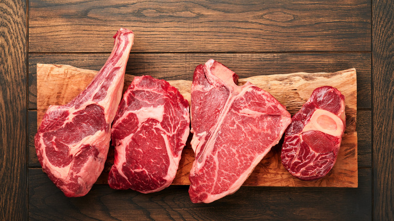 Four types of raw steak sit in a row on a wooden table