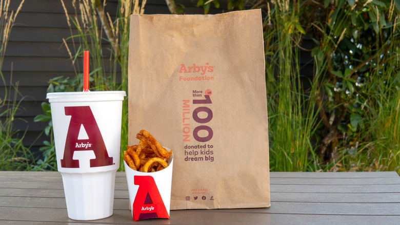 Arby's bag, drink, and curly fries on a table