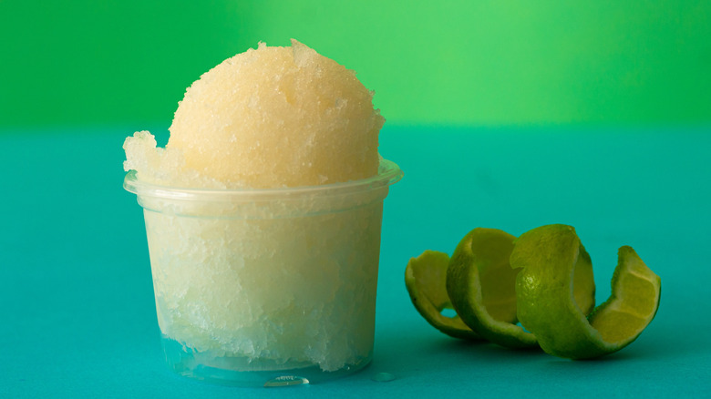 A clear cup of sorbet beside a curled lime rind.
