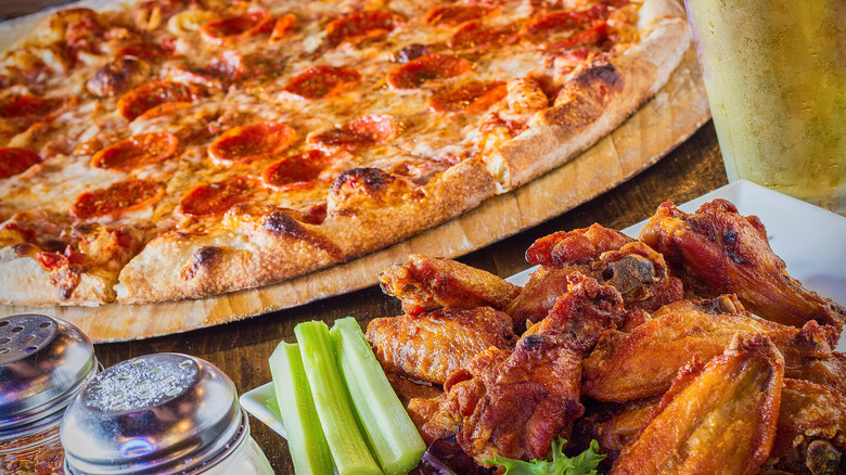 A plate of chicken wings and a pizza on a cutting board.