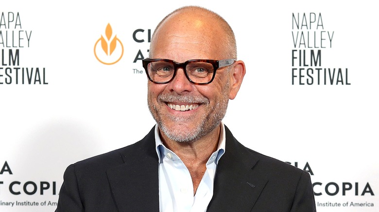 Alton Brown smiling wearing dark-rimmed glasses