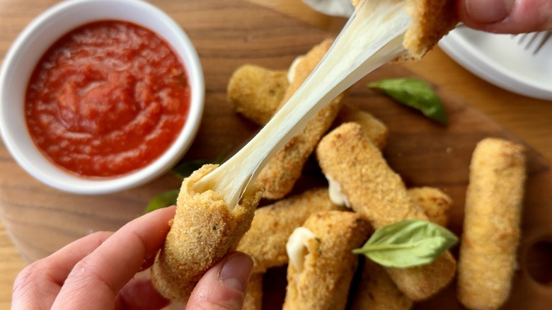 hand holding two parts of a mozzarella stick above a bowl of tomato sauce