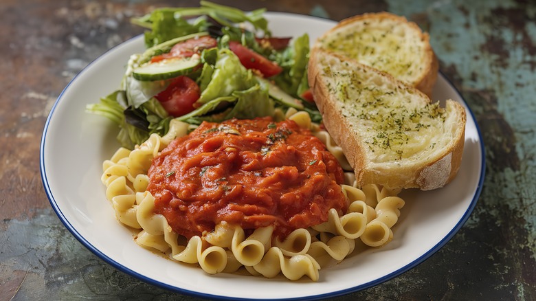 A plate of pasta covered in red sauce, a mixed greens salad above it, with toasted garlic bread to the side.