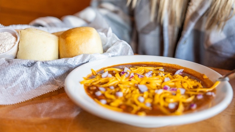 Woman with bowl of Texas Roadhouse chili next to basket of rolls
