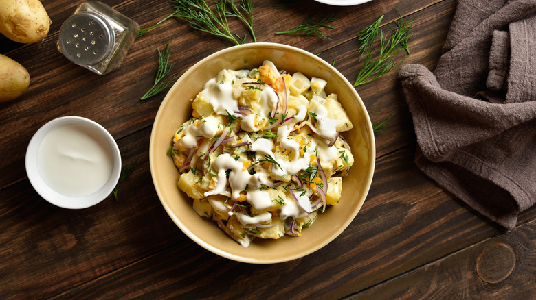 Potato salad with fresh ingredients on wooden table