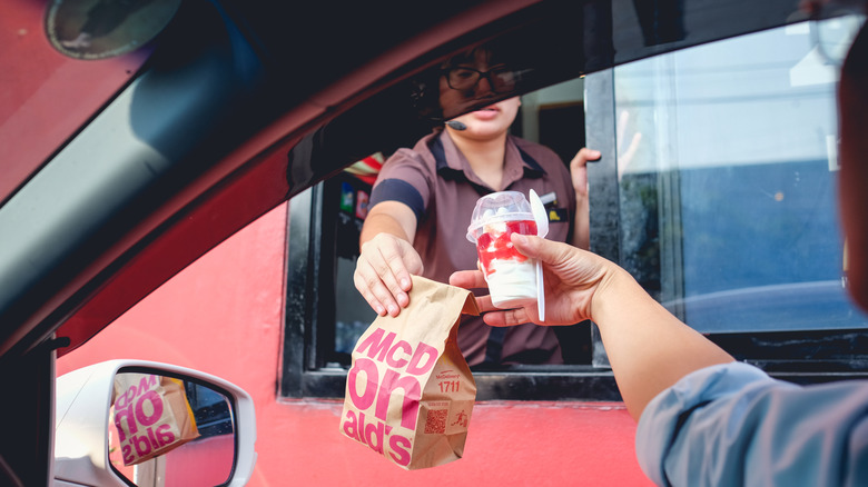 woman in drive-thru window hands customer McDonald's order