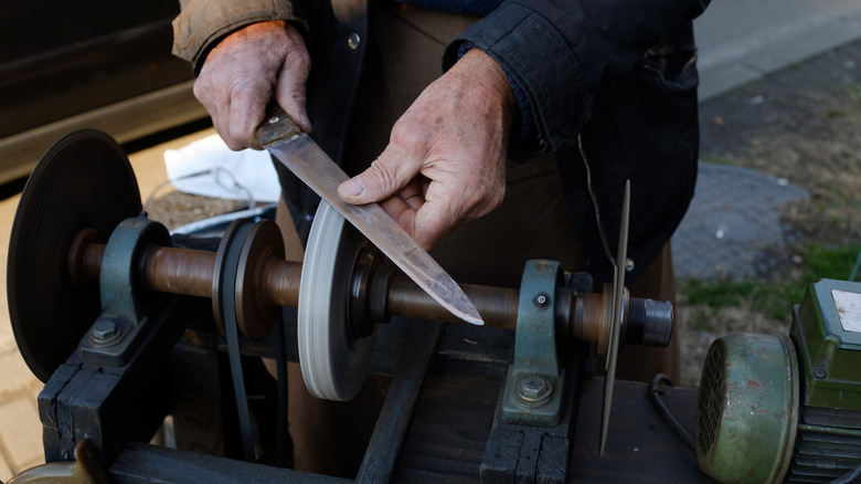 An older man sharpening a knife on an old-fashioned wheel grinder