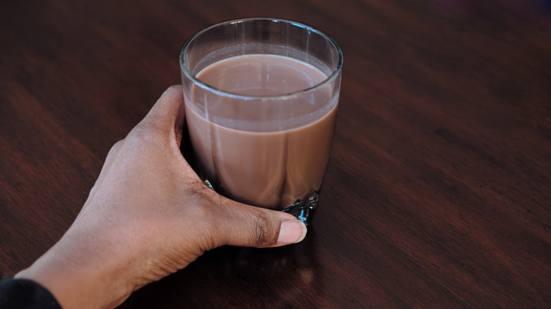 A hand cups a glass of chocolate milk