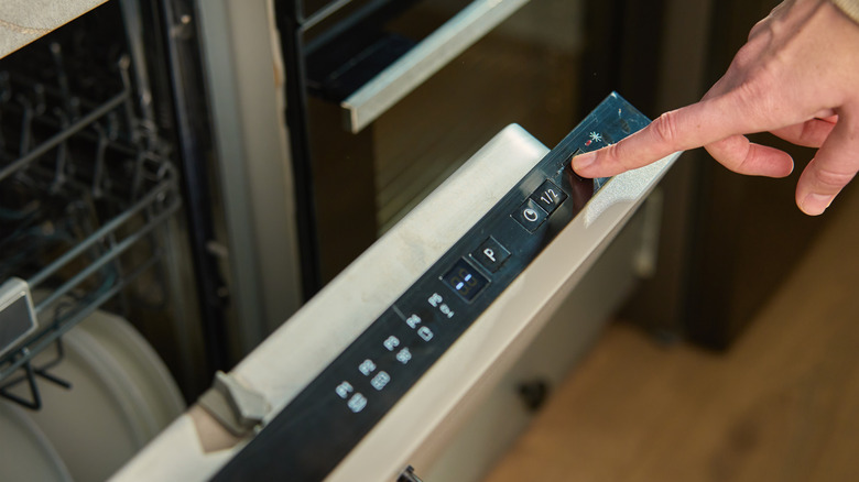 A finger pressing buttons on a dishwasher.