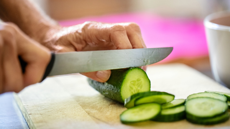 Slicing a cucumber on a wooden cutting board.