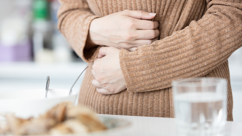 Person in a brown long sleeved shirt holds their stomach in pain