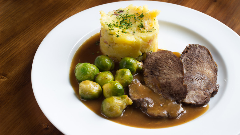 Beef neck gravy served with sides of mashed potatoes and Brussels sprouts