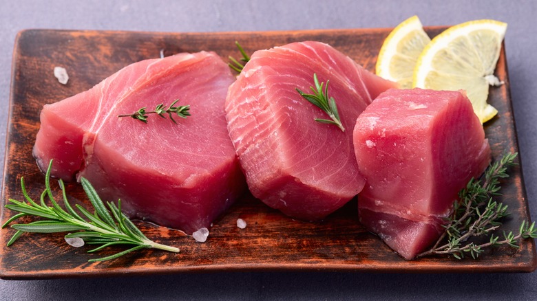 Raw tuna steaks on a wooden platter with lemon and herbs