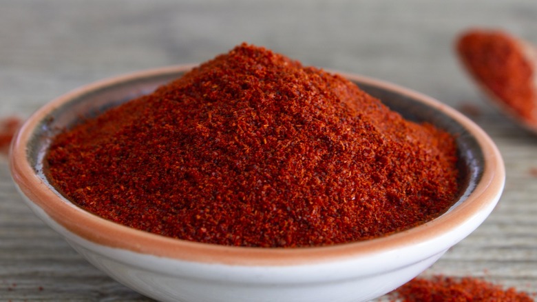 A heaping bowl of chili powder sits on a wooden table