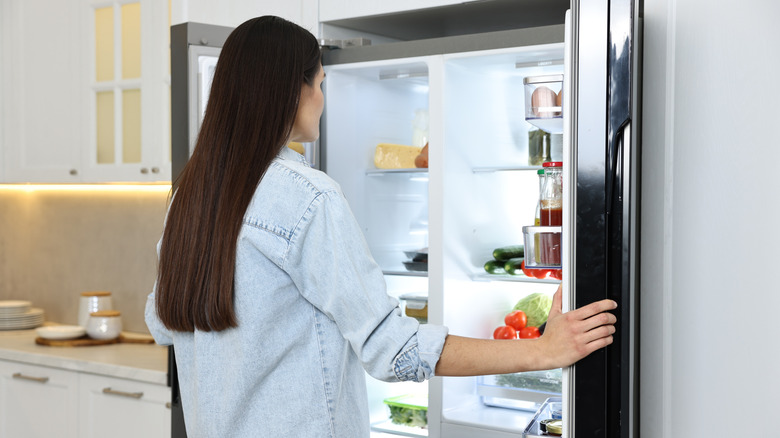 A person peers into a double doored refrigerator/freezer in a neutral kitchen