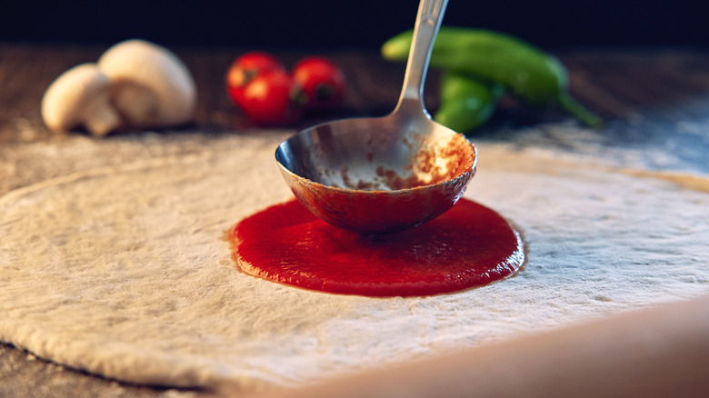 Person putting red sauce on pizza with scoop