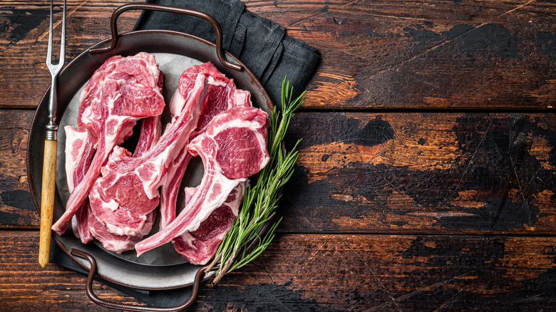Raw lamb chops sitting in a pan alongside rosemary
