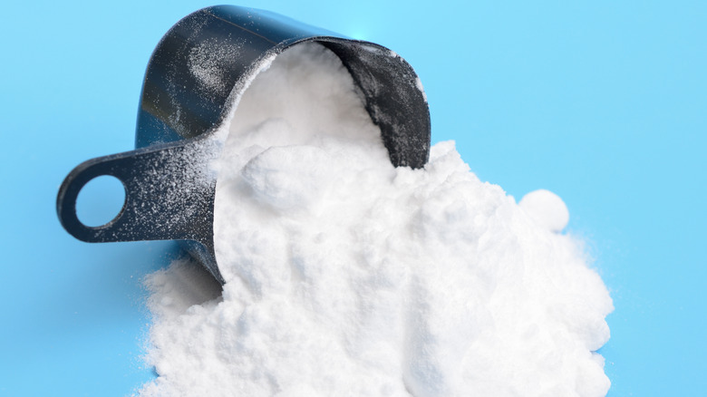 Pouring cream of tartar out of a measuring cup against blue background