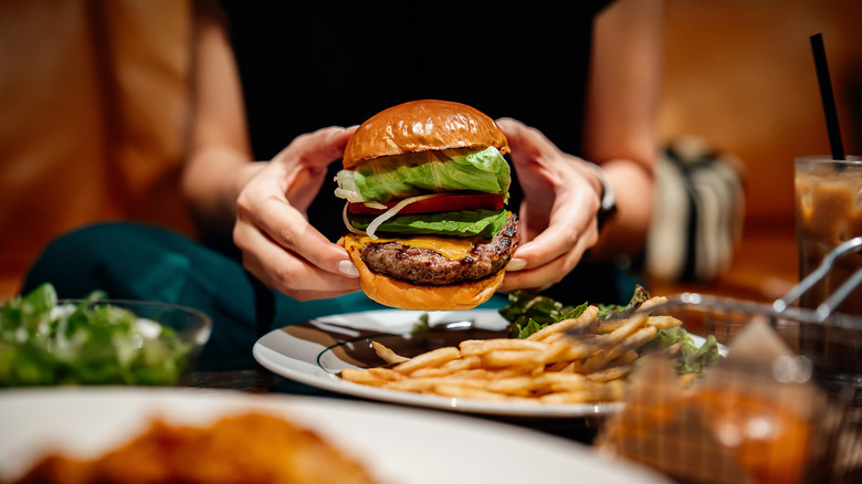 Person holding a cheeseburger with toppings