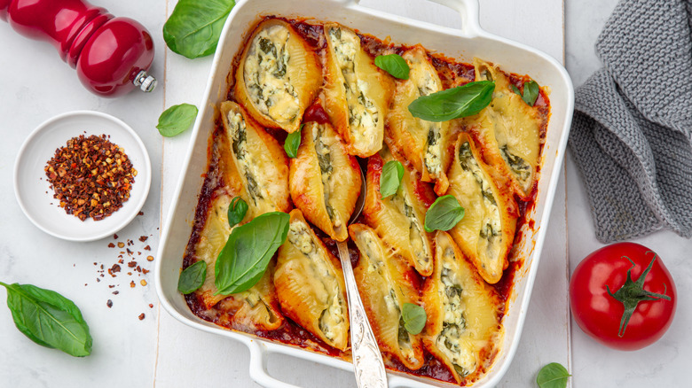 A white tray of stuffed shells with basil leaves and red pepper