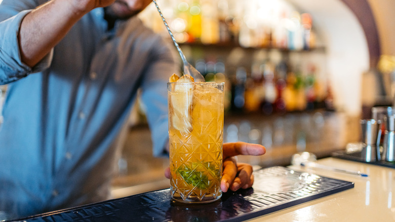 a bartender mixing a vibrant highball cocktail in a tall glass