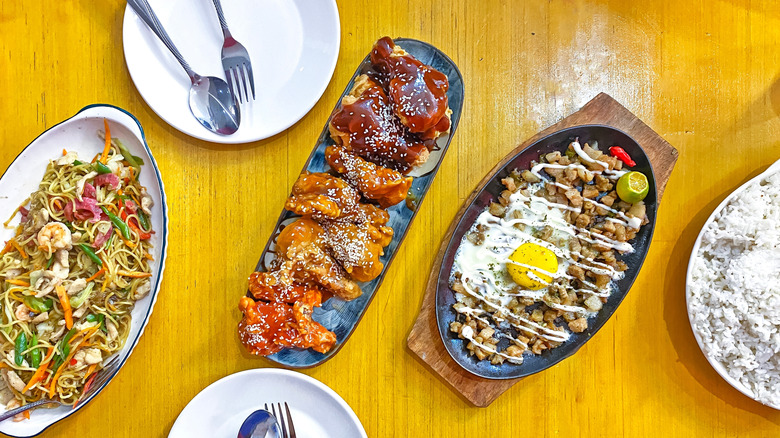 Sisig, pancit, chicken wings, and rice on table with plates