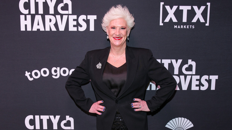 Anne Burrell posing in front of a media wall in a suit