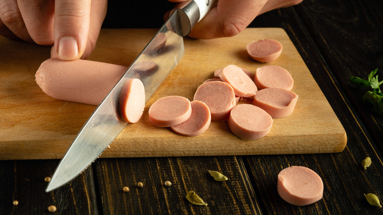 Slicing a Vienna sausage on a wooden cutting board