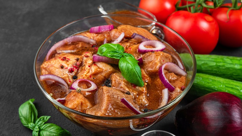 Cut pieces of meat marinating in a bowl with slices of red onion