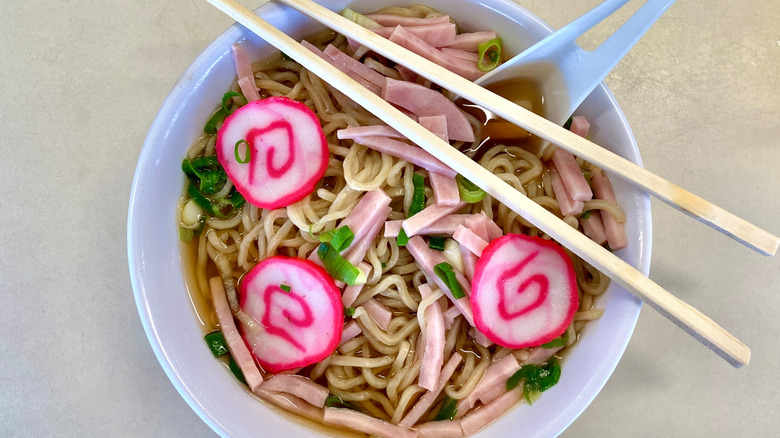 A bowl of saimin made with broth, noodles, fish cakes, meat, and scallions