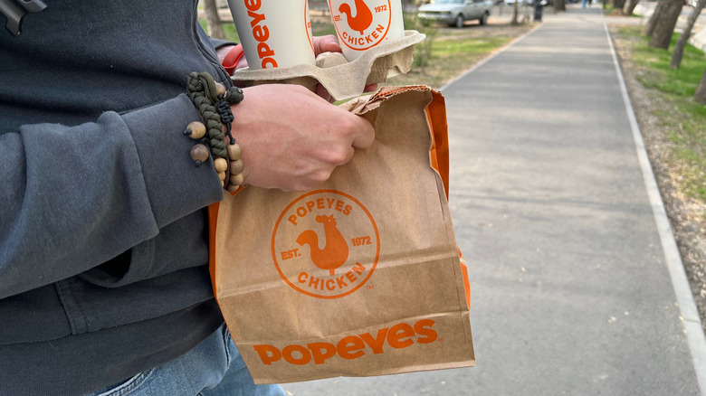 Person holding a Popeyes takeout bag and drinks