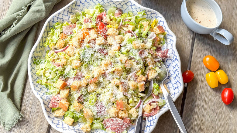Italian deli grinder salad in serving bowl on table with tomatoes and dressing