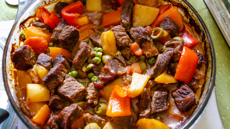 Close up glass bowl of kaldereta stew with peas and peppers