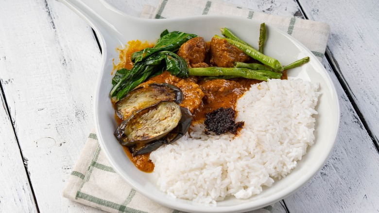 White bowl of kare-kare stew with eggplant and steamed rice