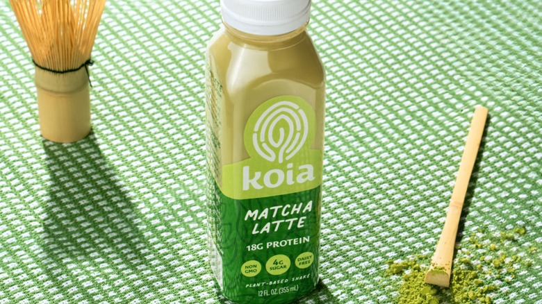 Koia Matcha Latte Protein Shake on green cloth with bamboo sticks and matcha powder