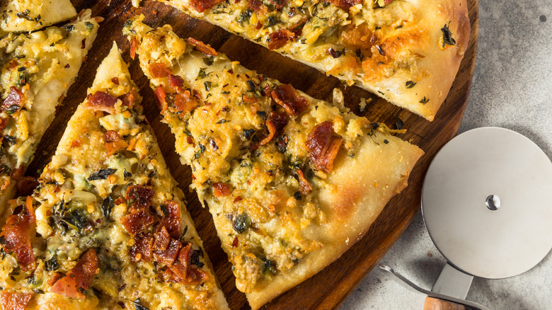 Clam and bacon pizza slices on a wooden board next to a pizza cutter